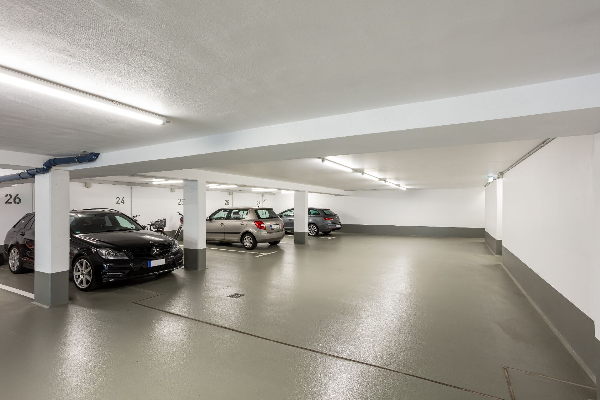 Helle Tiefgarage mit mehreren geparkten Autos und markierten Stellplätzen.