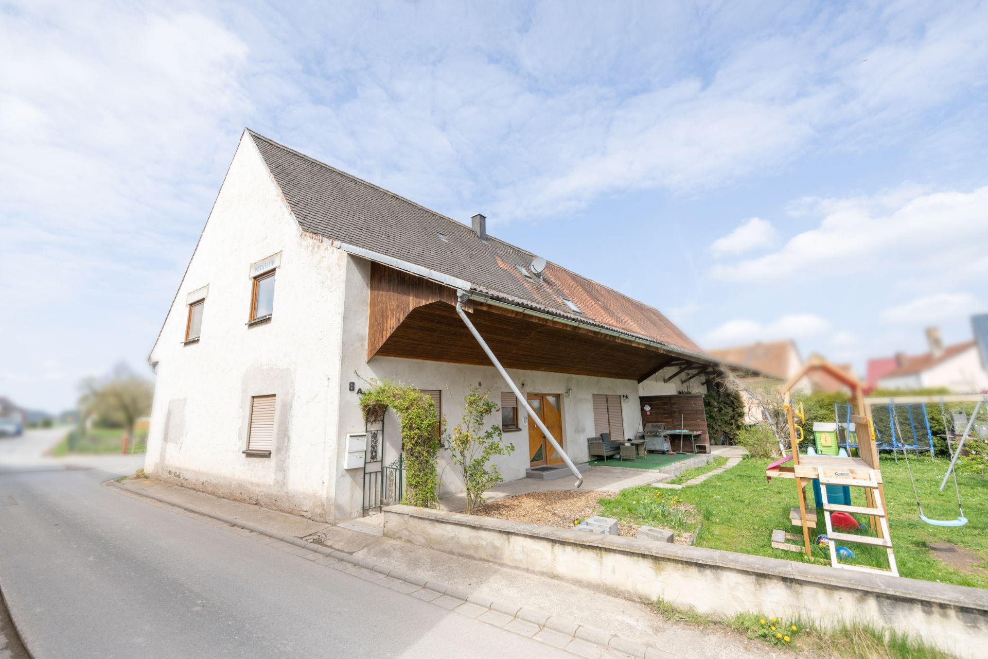 Großes Wohnhaus mit überdachter Terrasse und kleinem Garten mit Spielplatz auf der rechten Seite.