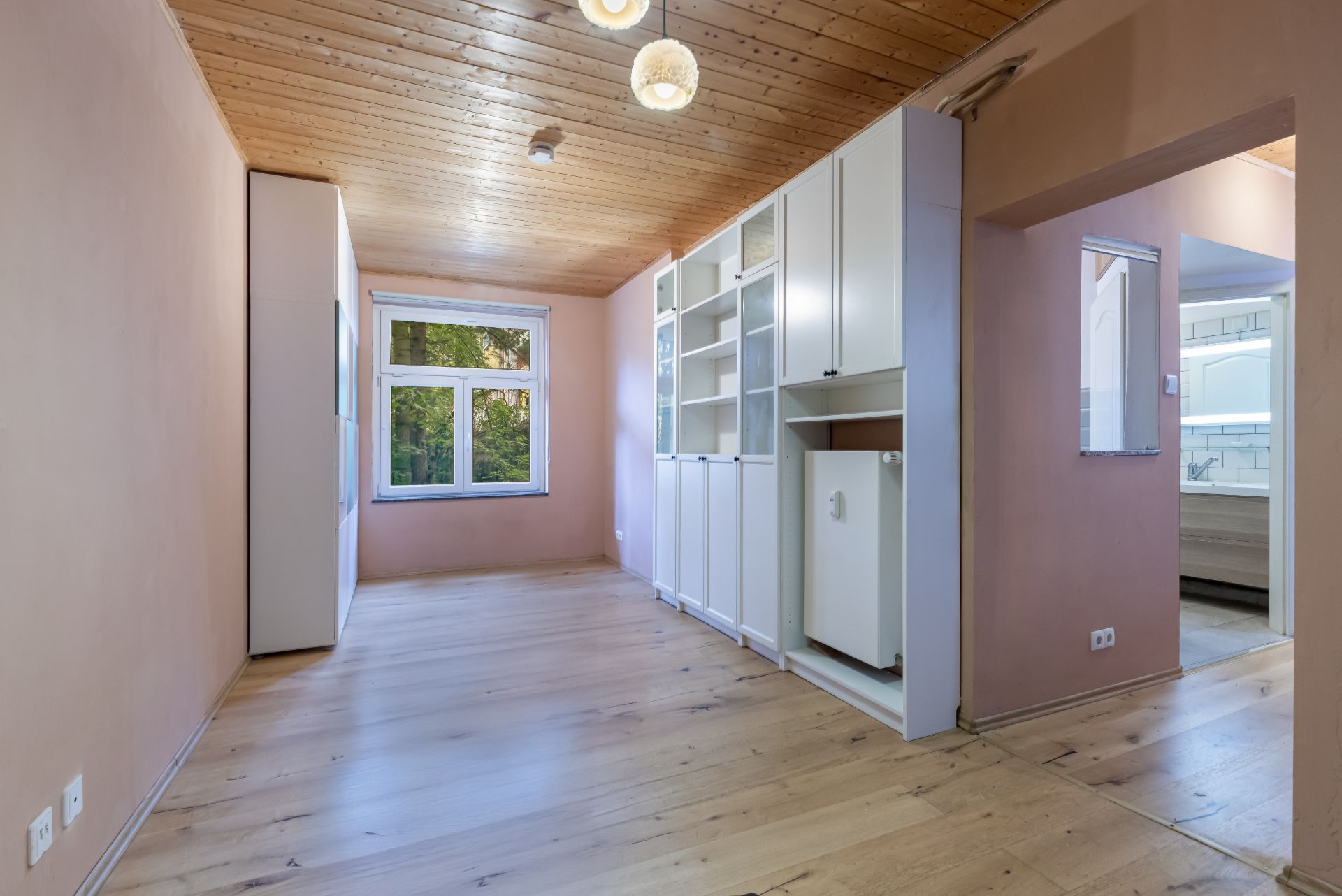 Helles Zimmer mit Holzdecke, großem Fenster und weißen Einbauschränken.