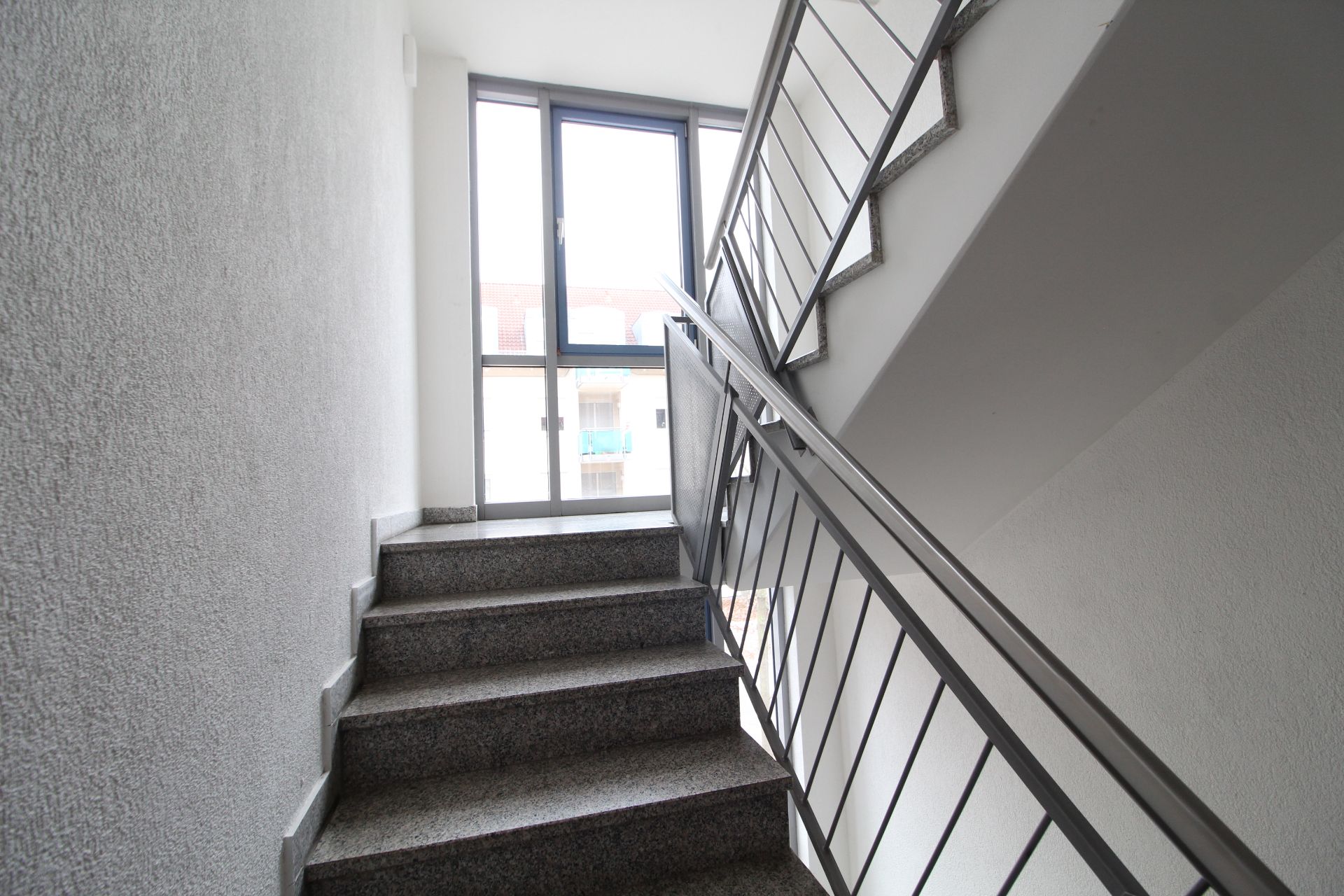 Helle Treppe mit Metallgeländer und Fenster am Ende im Wohngebäude.