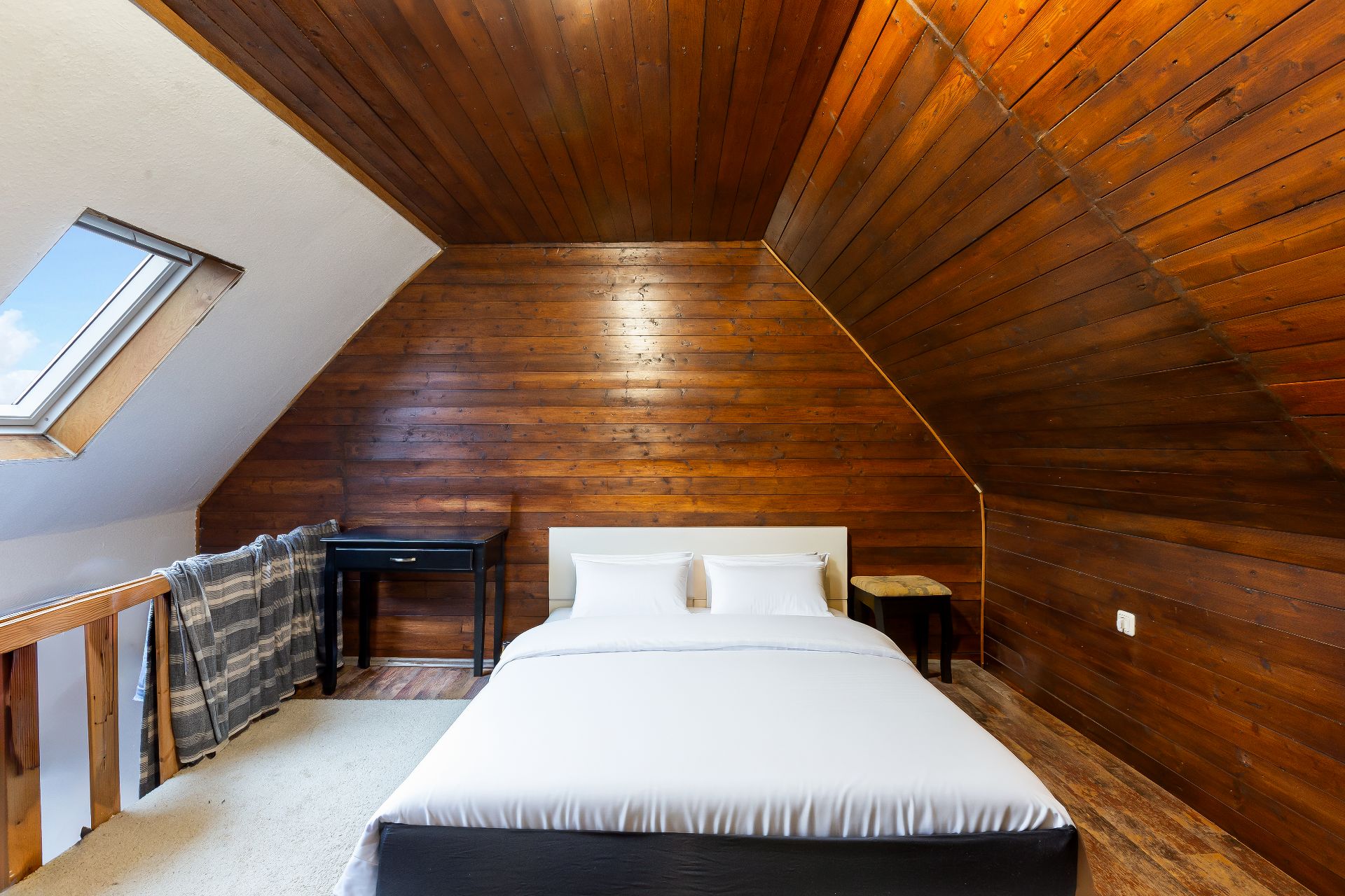 Schlafzimmer mit Holzwänden, Doppelbett, Schreibtisch und Dachfenster.