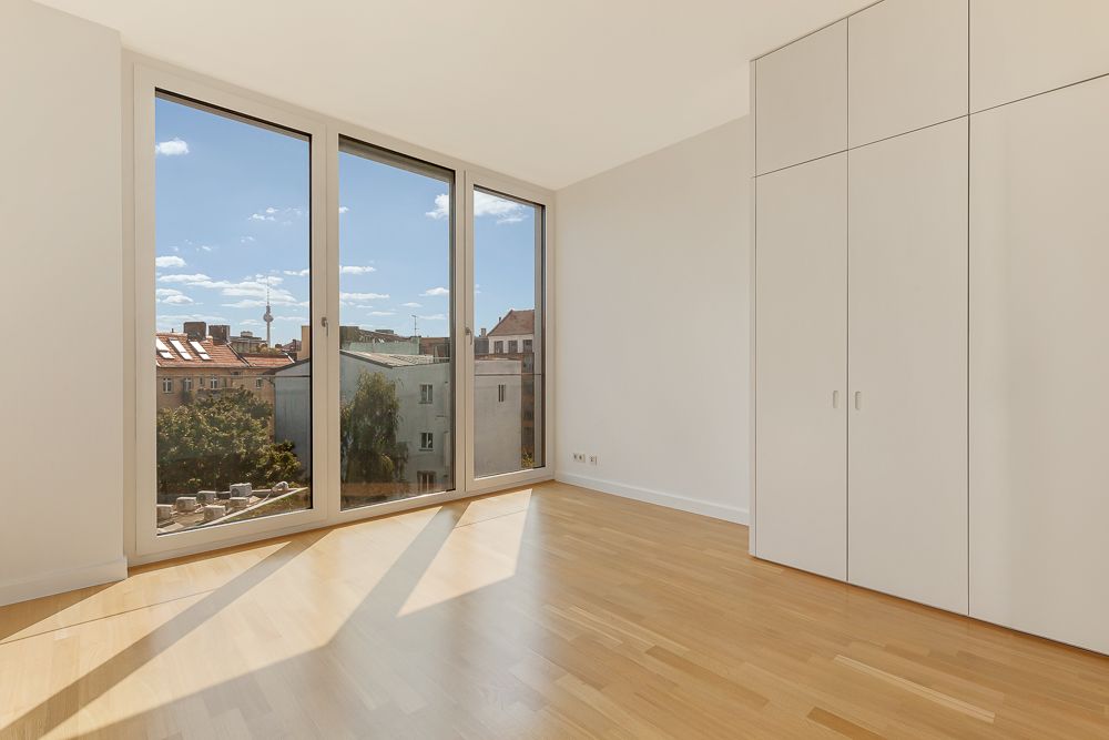Helles Zimmer mit großem Fenster, Holzboden und Einbauschrank, Blick auf Nachbargebäude.