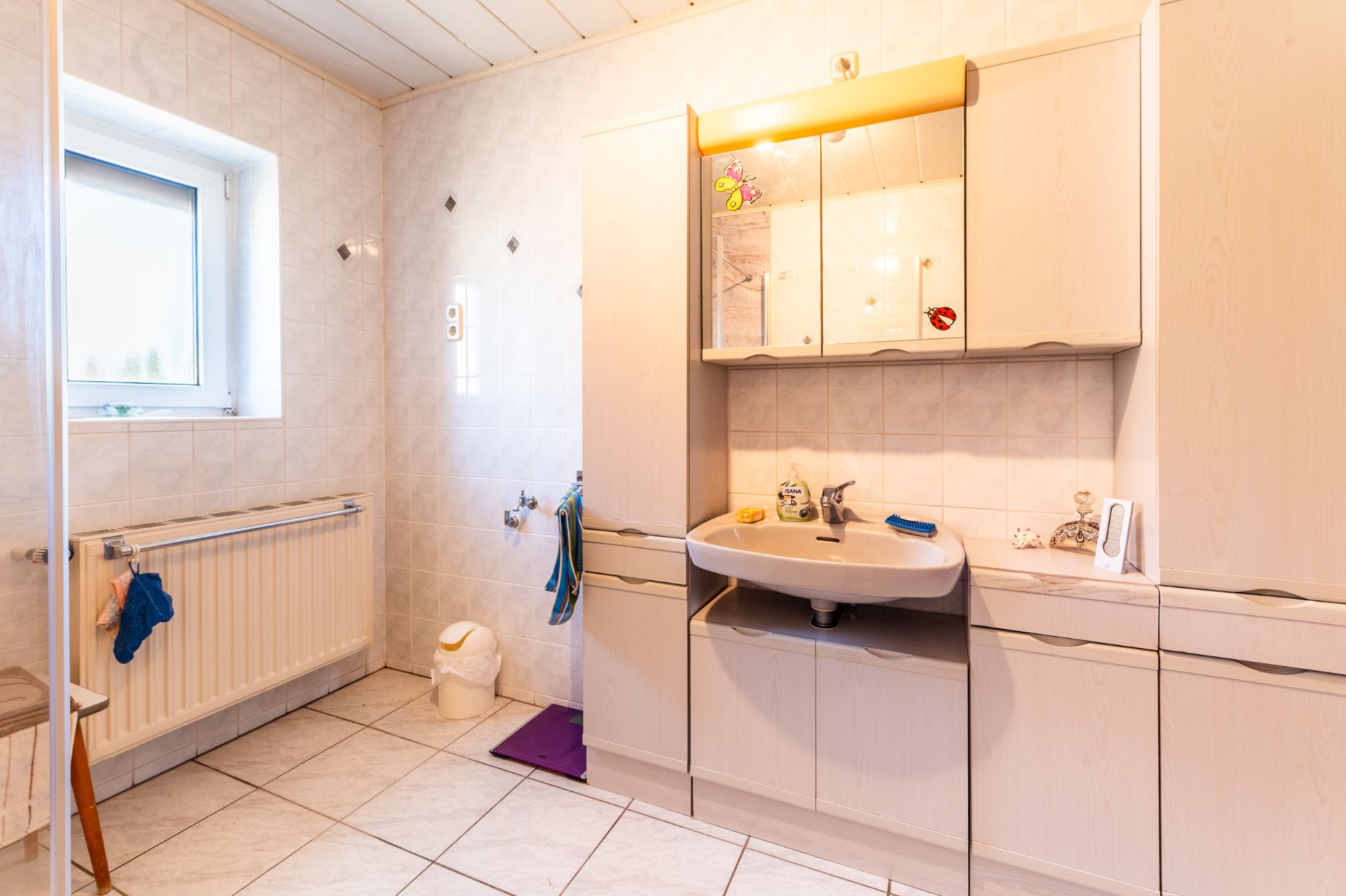 Helles Badezimmer mit großem Waschbecken, Spiegelschrank und Fenster.