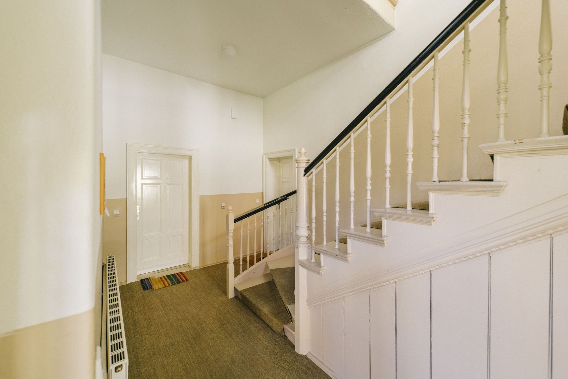 Heller Flur mit Teppich, zwei weißen Türen und Treppe mit weißem Geländer.