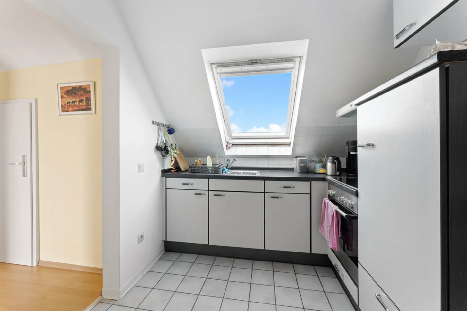 Helle Einbauküche mit Dachfenster, weißen Schränken und Fliesenfußboden.