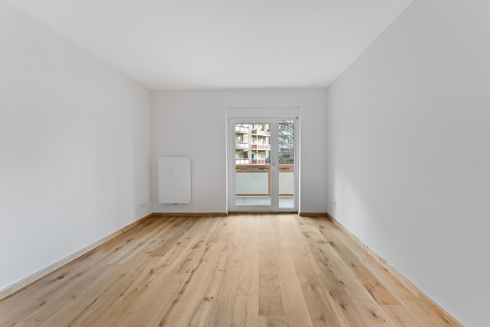 Leerer Raum mit Holzfußboden, weißem Heizkörper und Glastür zu einem Balkon.