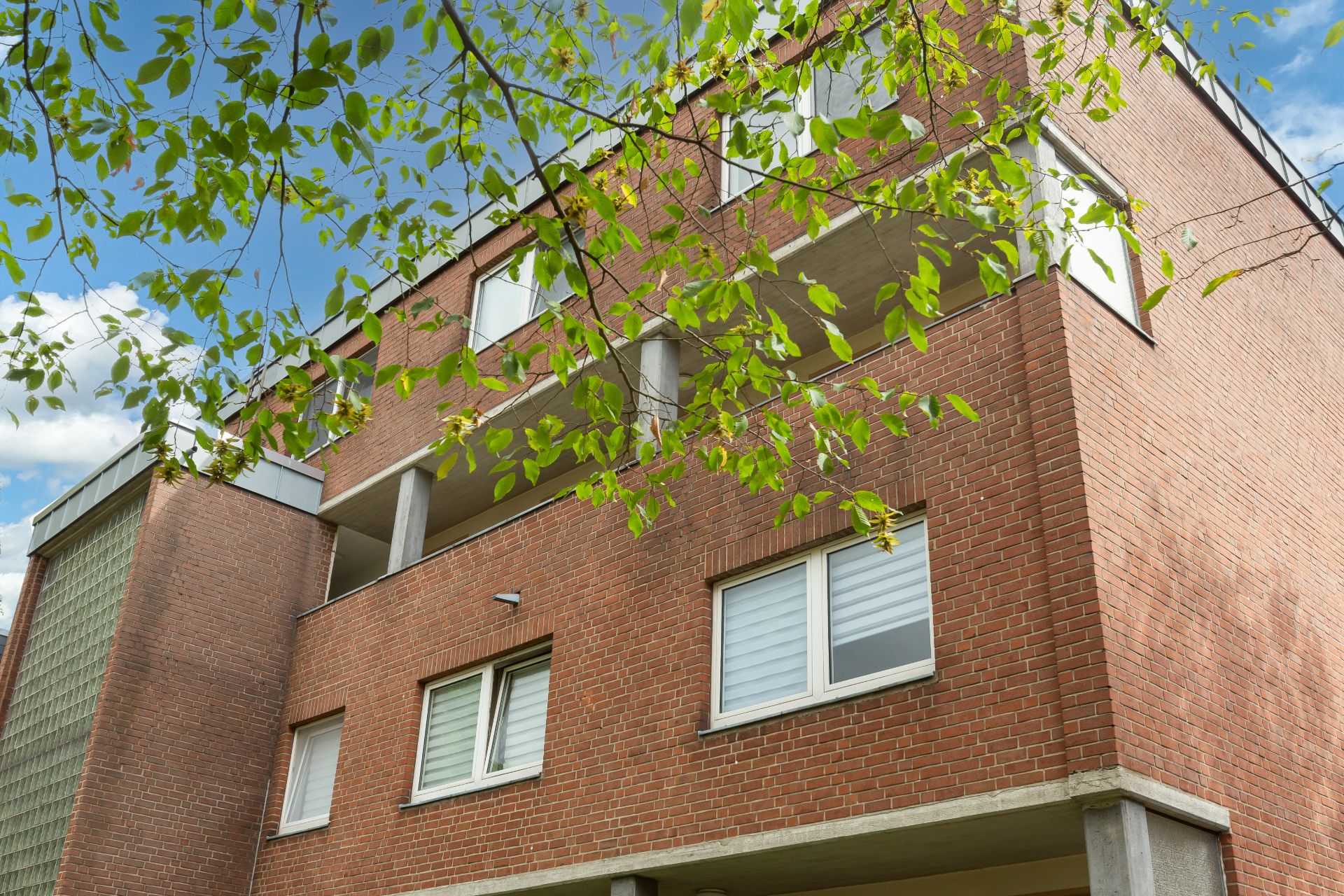 Mehrstöckiges Wohnhaus aus rotem Backstein mit Balkonen und Fenstern, Baumzweige im Vordergrund.