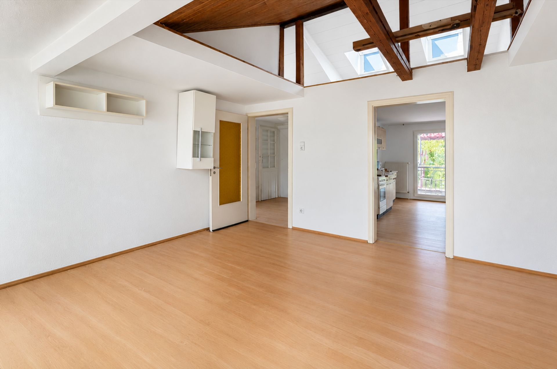 Helles Zimmer mit Holzdecke, sichtbaren Balken, Parkettboden und zwei offenen Türen zu weiteren Räumen.