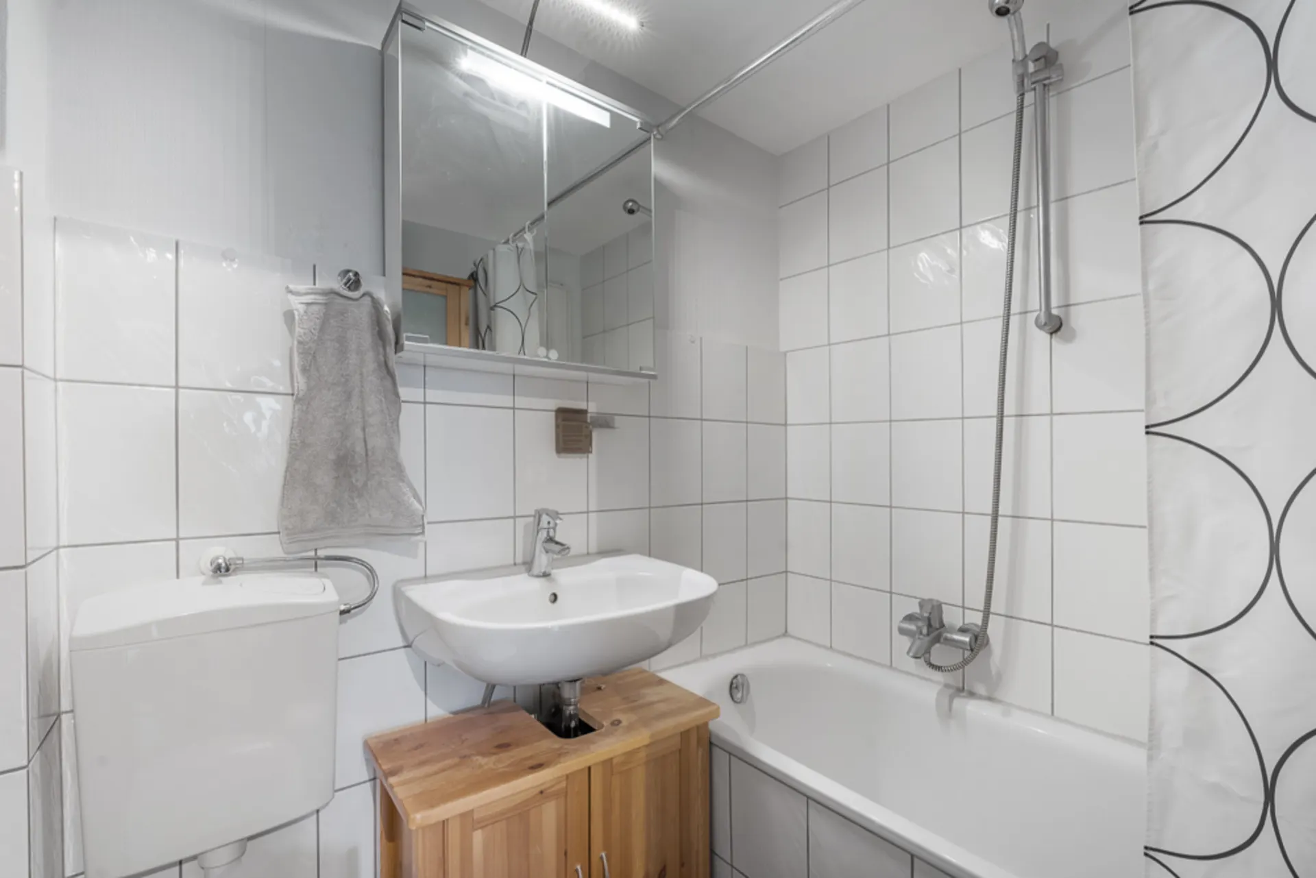 Kleines Badezimmer mit weiß gefliesten Wänden, Waschbecken, Toilette und Badewanne mit Duschvorhang.