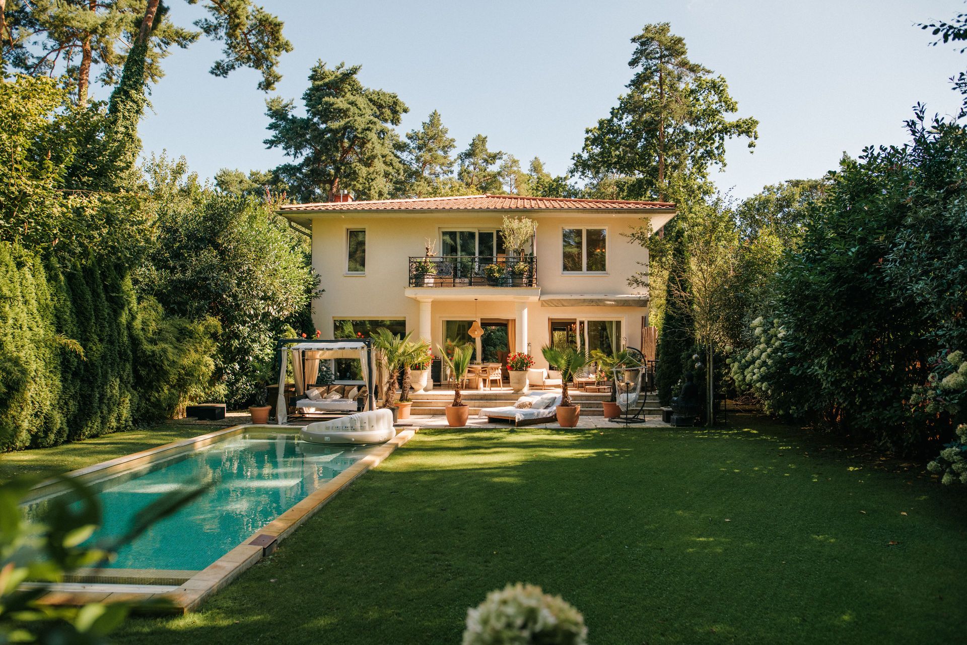 Modernes zweistöckiges Haus mit großem Garten und Pool, umgeben von Bäumen und Gartenmöbeln.