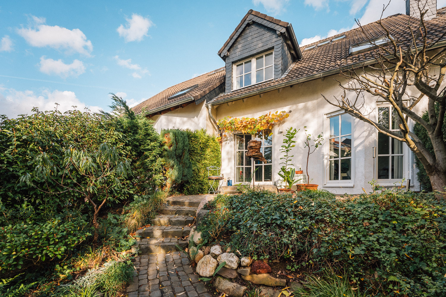 Einfamilienhaus mit Garten, Pflanzen und gepflastertem Weg bei sonnigem Wetter.