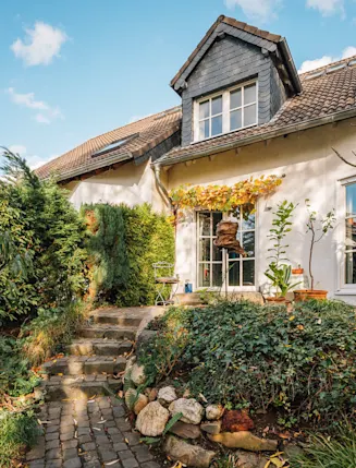 Einfamilienhaus mit Garten, Pflanzen und gepflastertem Weg bei sonnigem Wetter.