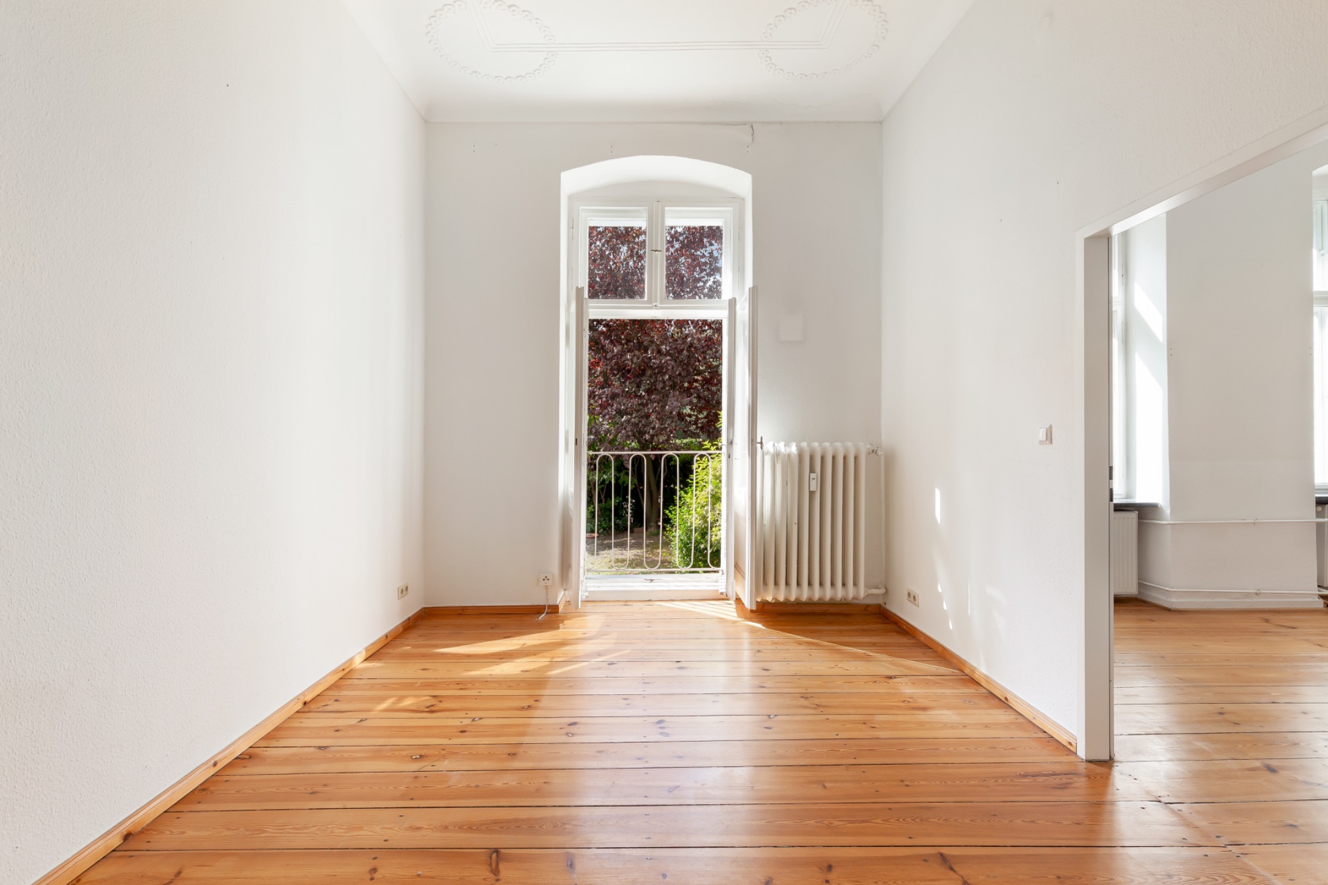 Helles Zimmer mit Holzboden, großem Fenster und Blick auf einen Garten.