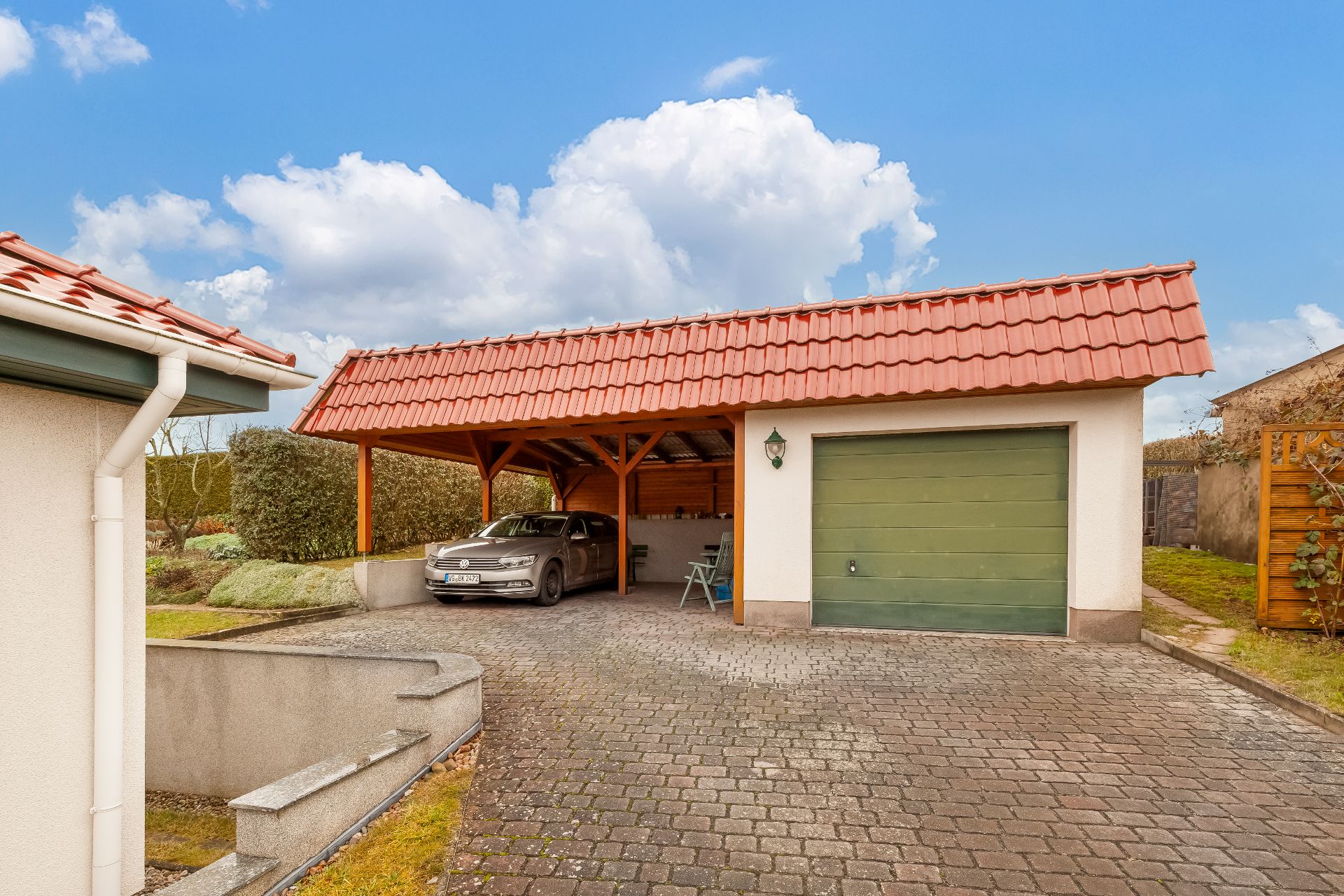Carport mit Auto und angrenzender Garage mit grünem Tor vor einem Wohnhaus.