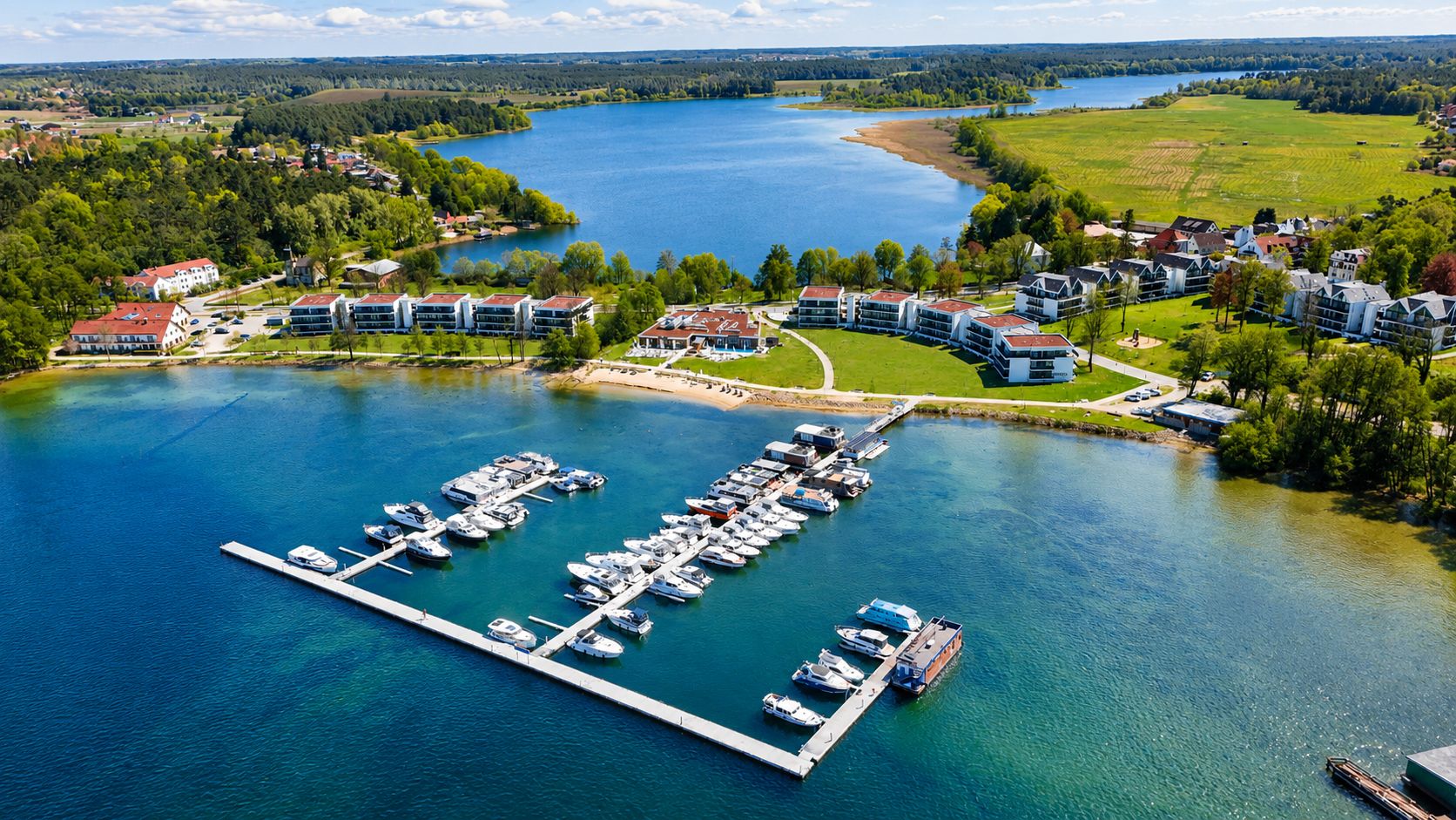 Luftaufnahme von Wohnhäusern am See mit Bootssteg und mehreren Booten im Wasser.
