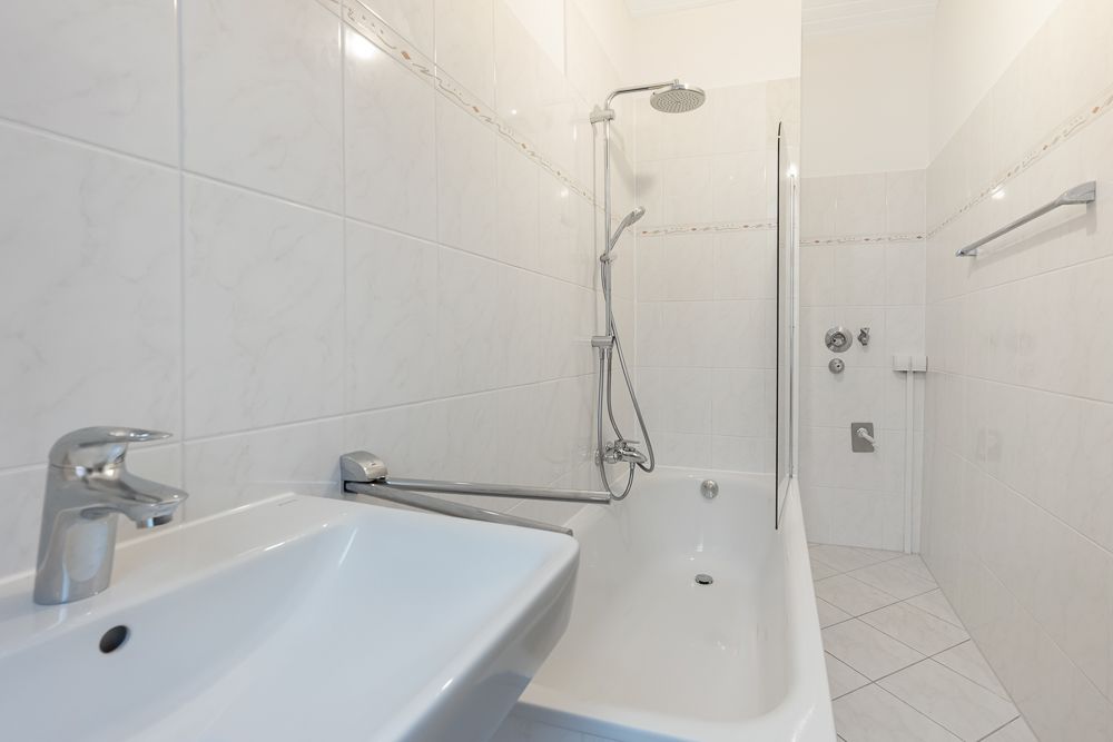 Helles Badezimmer mit Waschbecken, Badewanne und Dusche, weiße Fliesen an Wand und Boden.