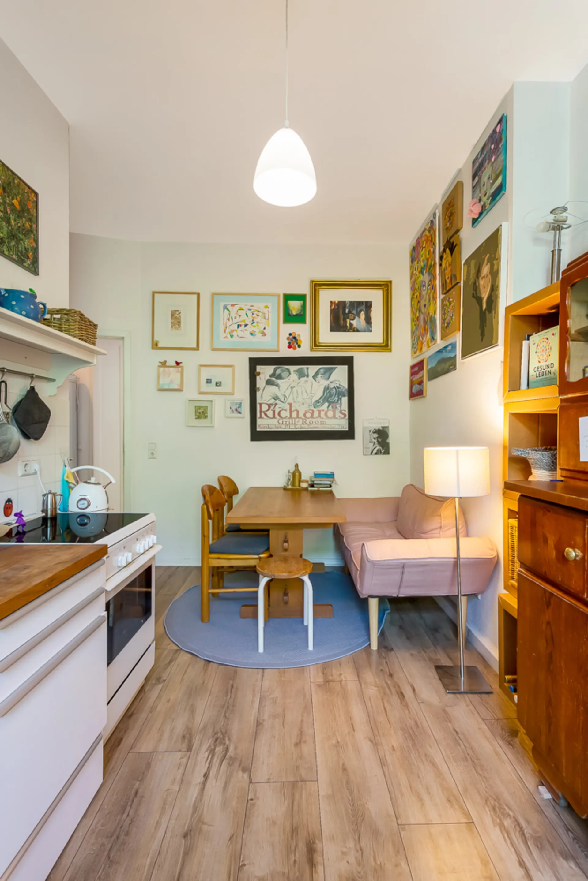 Kleine Wohnküche mit Esstisch, rosa Sofa, Holzstühlen und Wand mit Bildern.