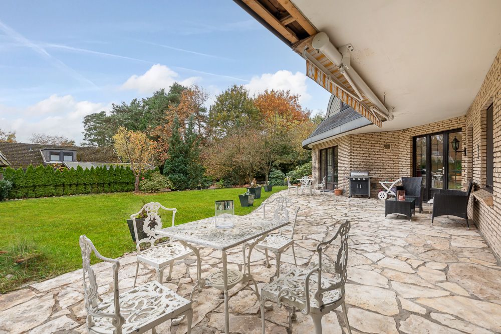 Große Steinterrasse mit weißen Gartenmöbeln und Blick auf einen grünen Garten.