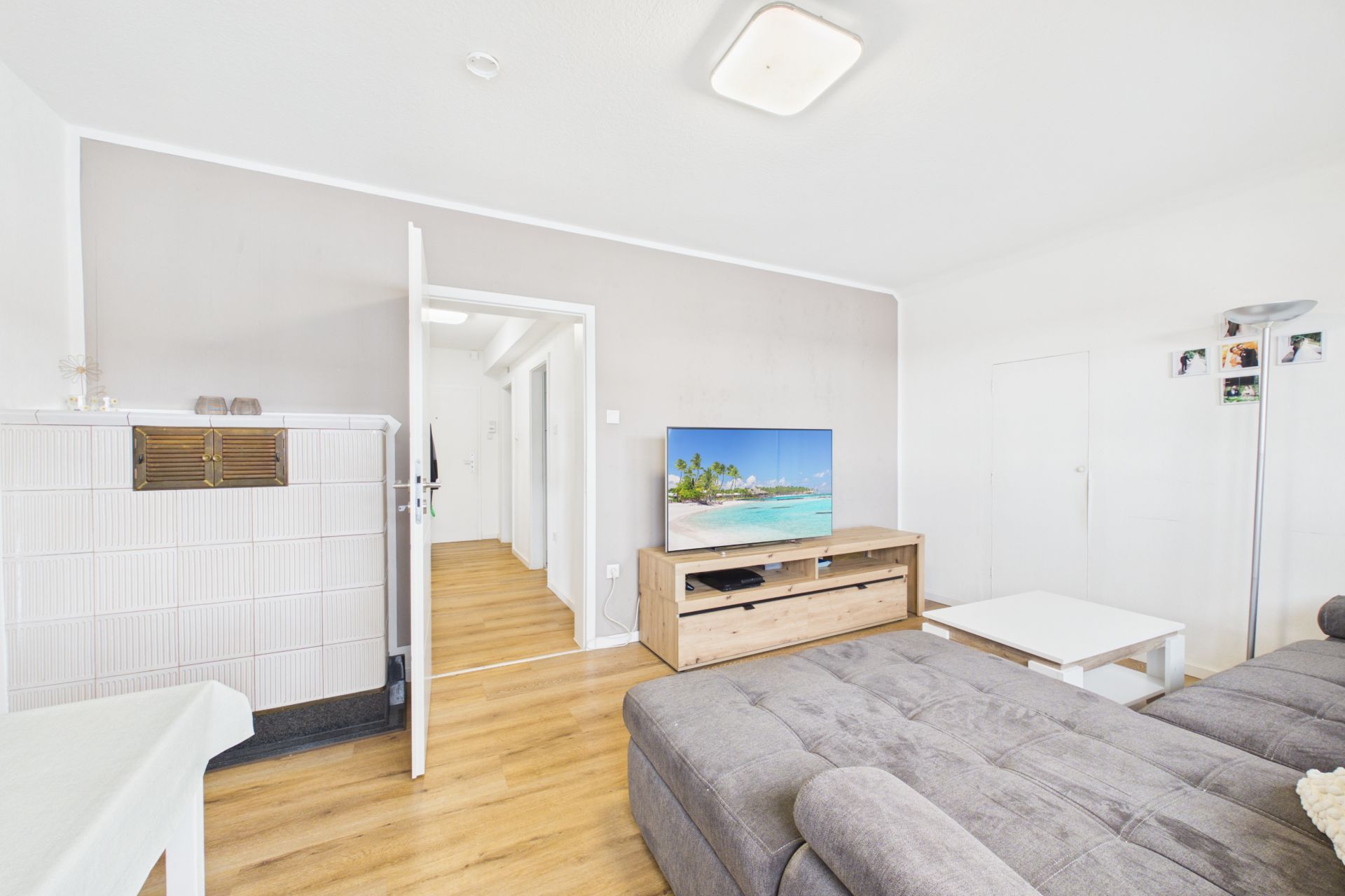 Helles Wohnzimmer mit grauem Sofa, Fernseher auf Holzschrank und Holzboden.