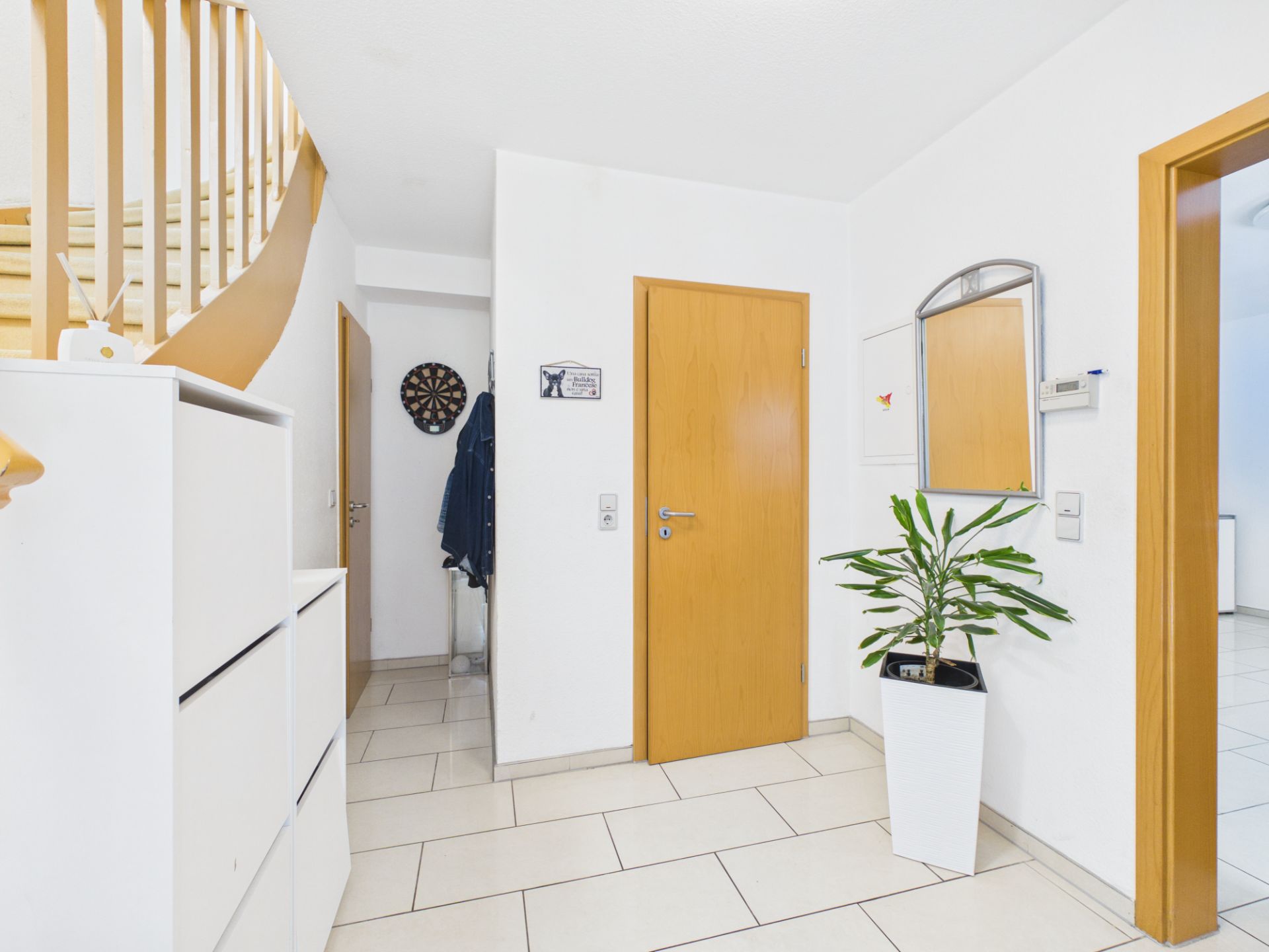 Heller Flur mit Holztreppe, Pflanze im weißen Topf, Spiegel und Schuhschrank.