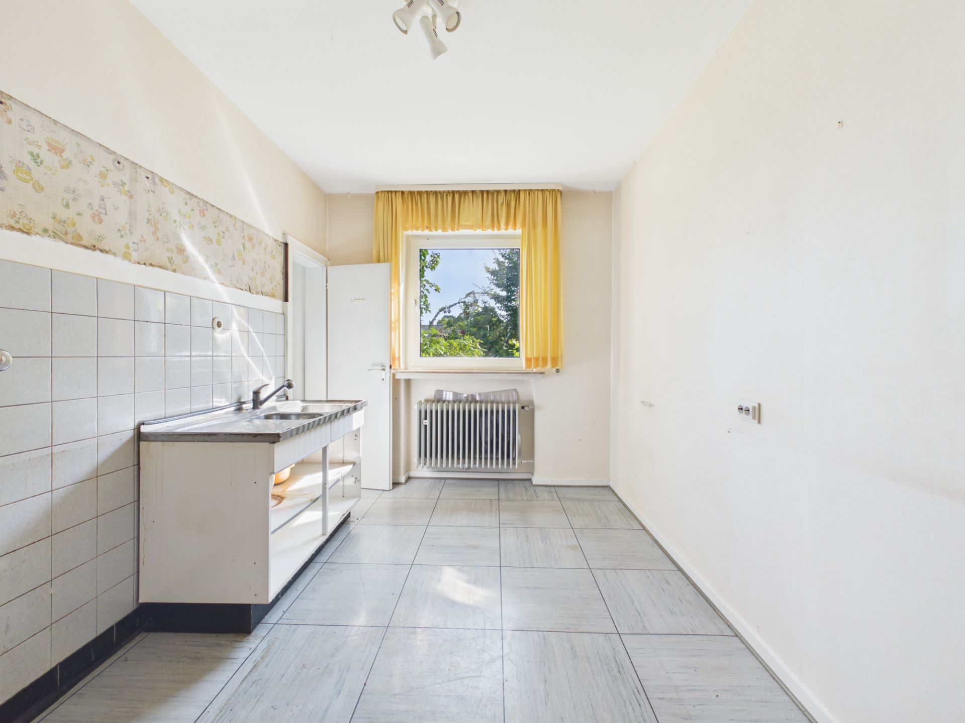 Helle, leere Küche mit gelbem Vorhang, Fenster und Spüle.