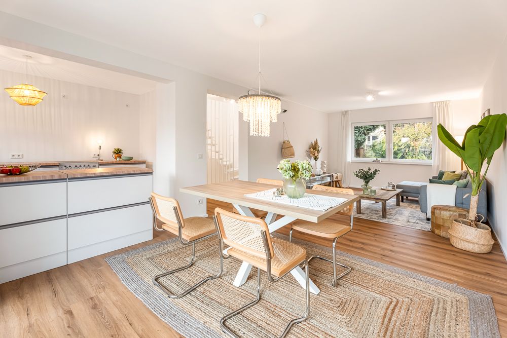 Helles Wohn- und Esszimmer mit Holzboden, Esstisch, moderner Küche und großer Pflanze.