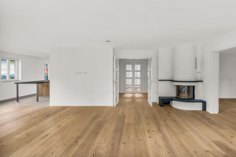 Helles Wohnzimmer mit Holzfußboden, Kamin und Blick auf Essbereich mit Fenstern.