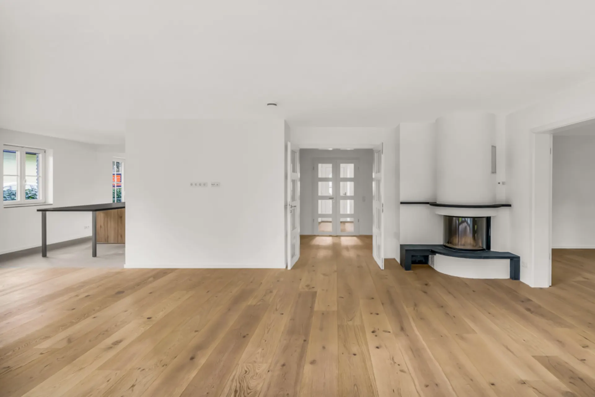 Helles Wohnzimmer mit Holzfußboden, Kamin und Blick auf Essbereich mit Fenstern.