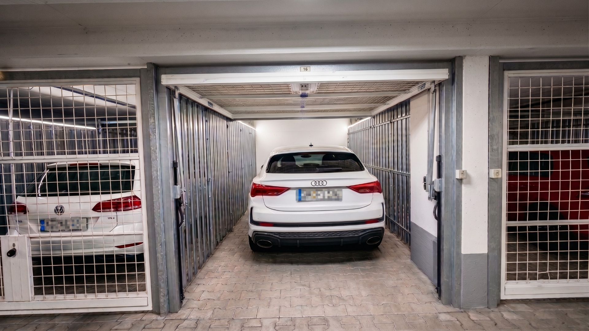 Weiße Autos stehen in abgeschlossenen Gittergaragen in einer Tiefgarage.