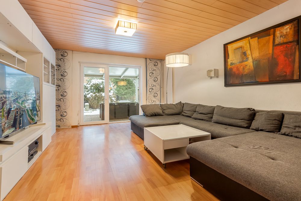 Wohnzimmer mit großer grauer Eckcouch, Couchtisch, TV und Zugang zur Terrasse.
