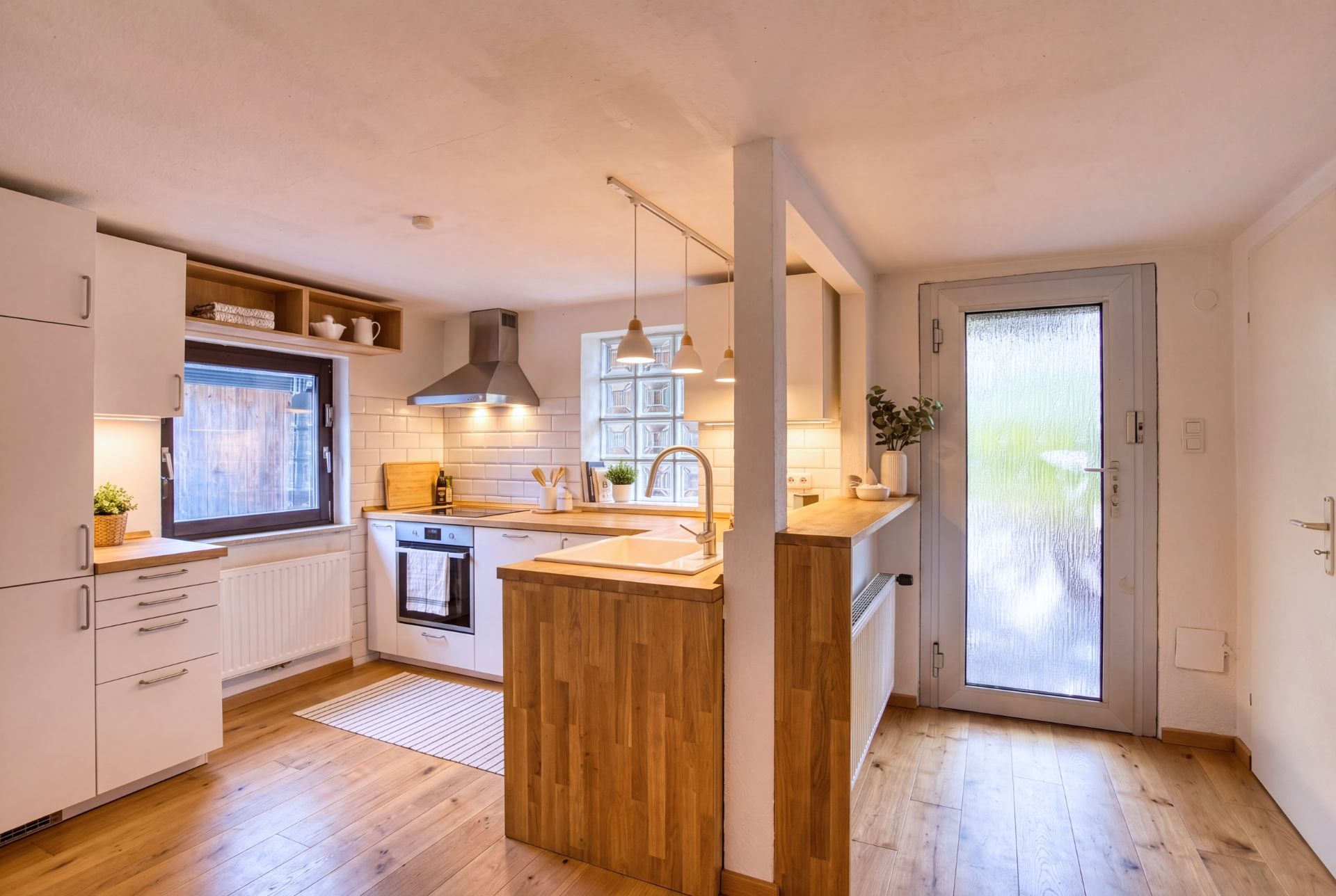 Moderne Küche mit weißen Schränken, Holzarbeitsplatte und großem Fenster neben einer Glastür.