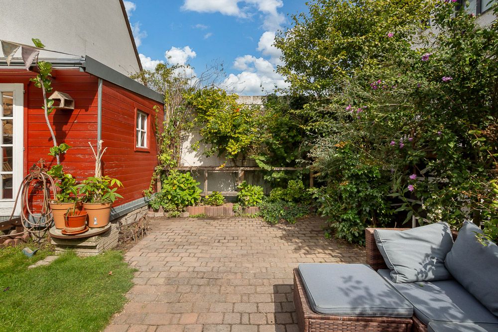 Kleiner gepflasterter Innenhof mit Sofa, Pflanzen und roten Hauswänden.