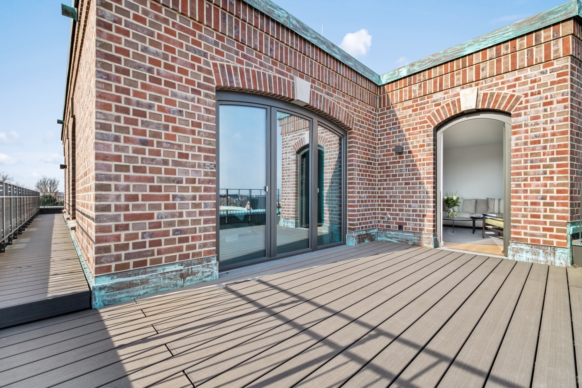 Große Dachterrasse mit Holzbelag und Backsteinfassade, zwei Zugänge ins Innere.