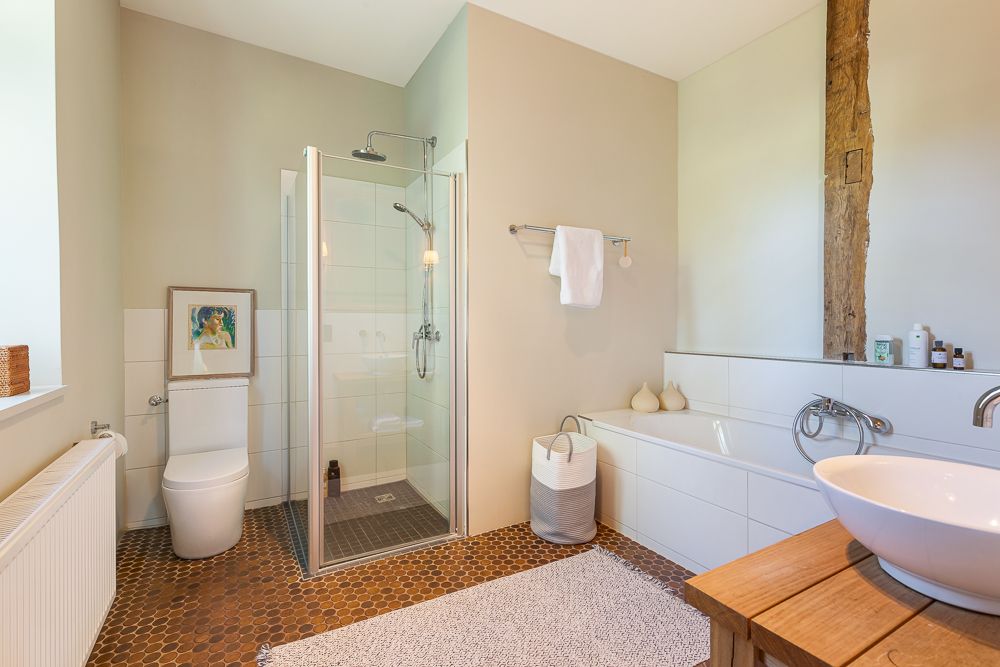 Modernes Badezimmer mit Dusche, Badewanne, Toilette und Waschbecken auf Holzkommode.