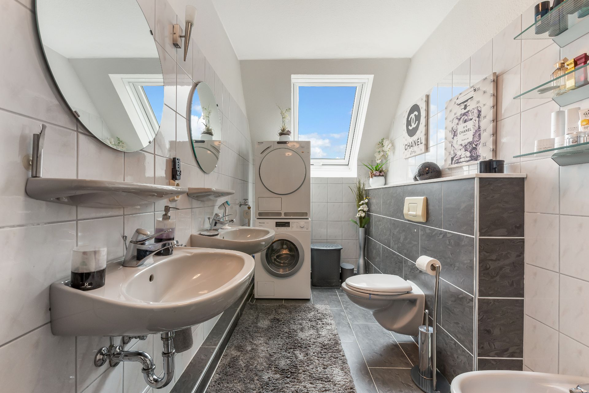 Modernes Badezimmer mit zwei Waschbecken, Toilette, Waschmaschine und Trockner unter Dachfenstern.