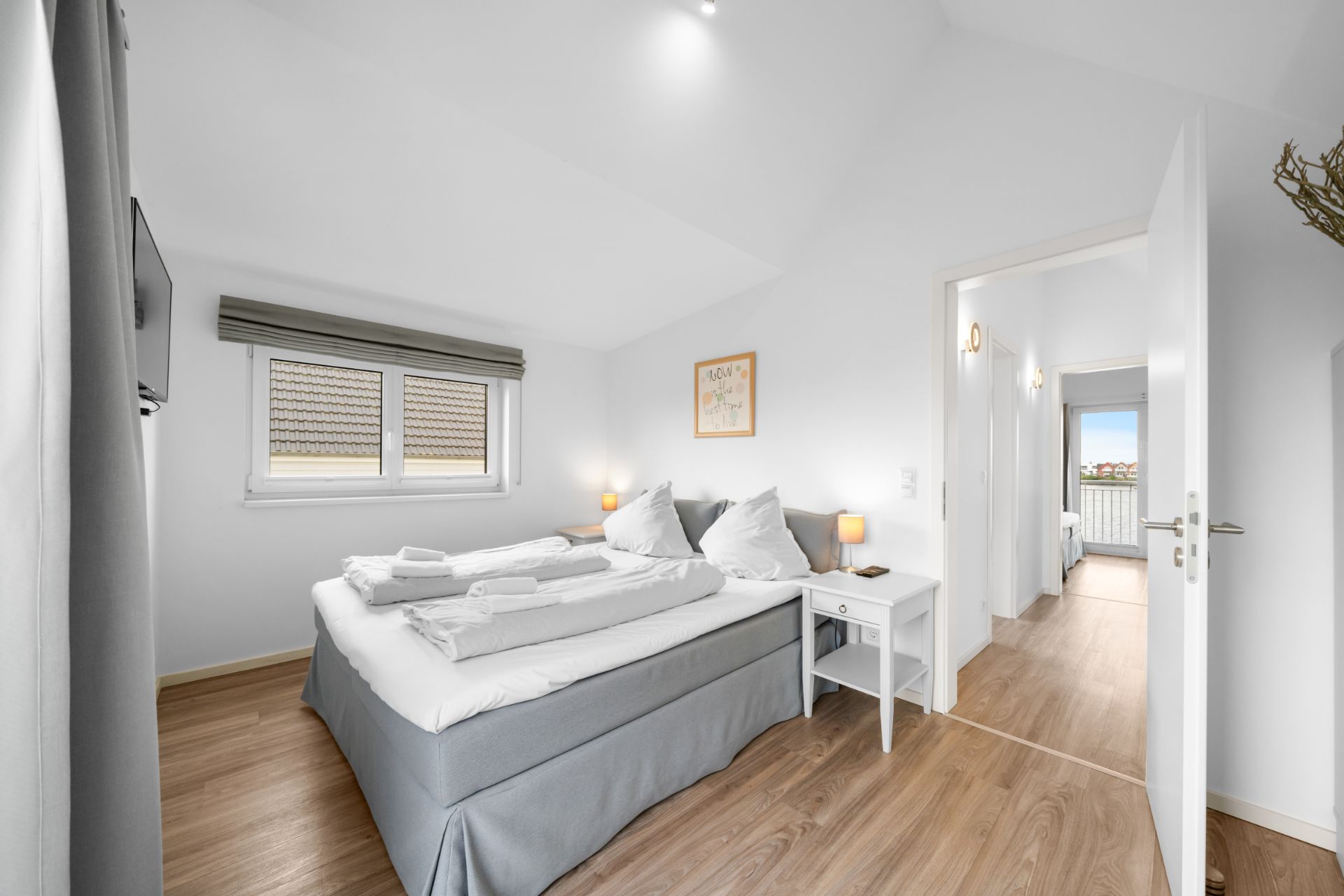 Helles Schlafzimmer mit Doppelbett, zwei Nachttischen, Holzfußboden und einem Fenster.