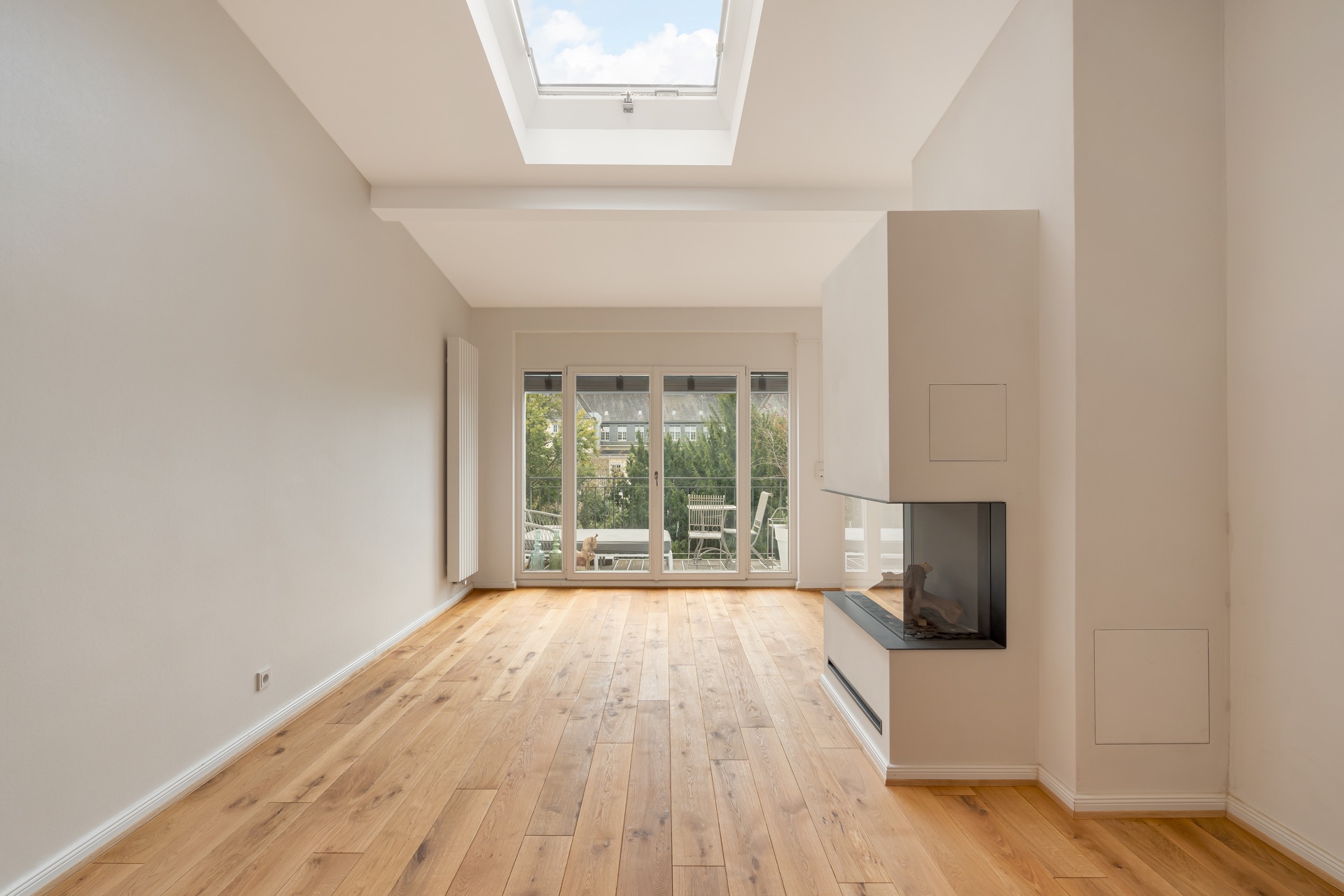 Helles Wohnzimmer mit Parkettboden, Kamin, Dachfenster und großer Glasfront zur Terrasse.