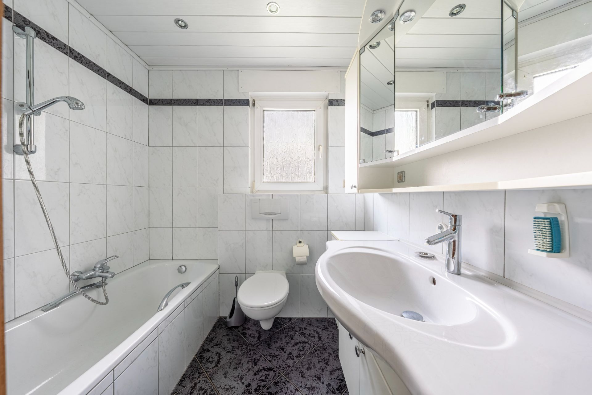 Helles Badezimmer mit Badewanne, Toilette, Waschbecken und Spiegelschrank.