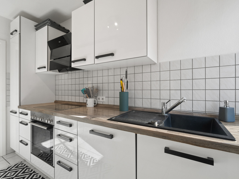 Moderne Küche mit weißen Schränken, Herd, Spüle und Küchenutensilien auf der Arbeitsfläche.