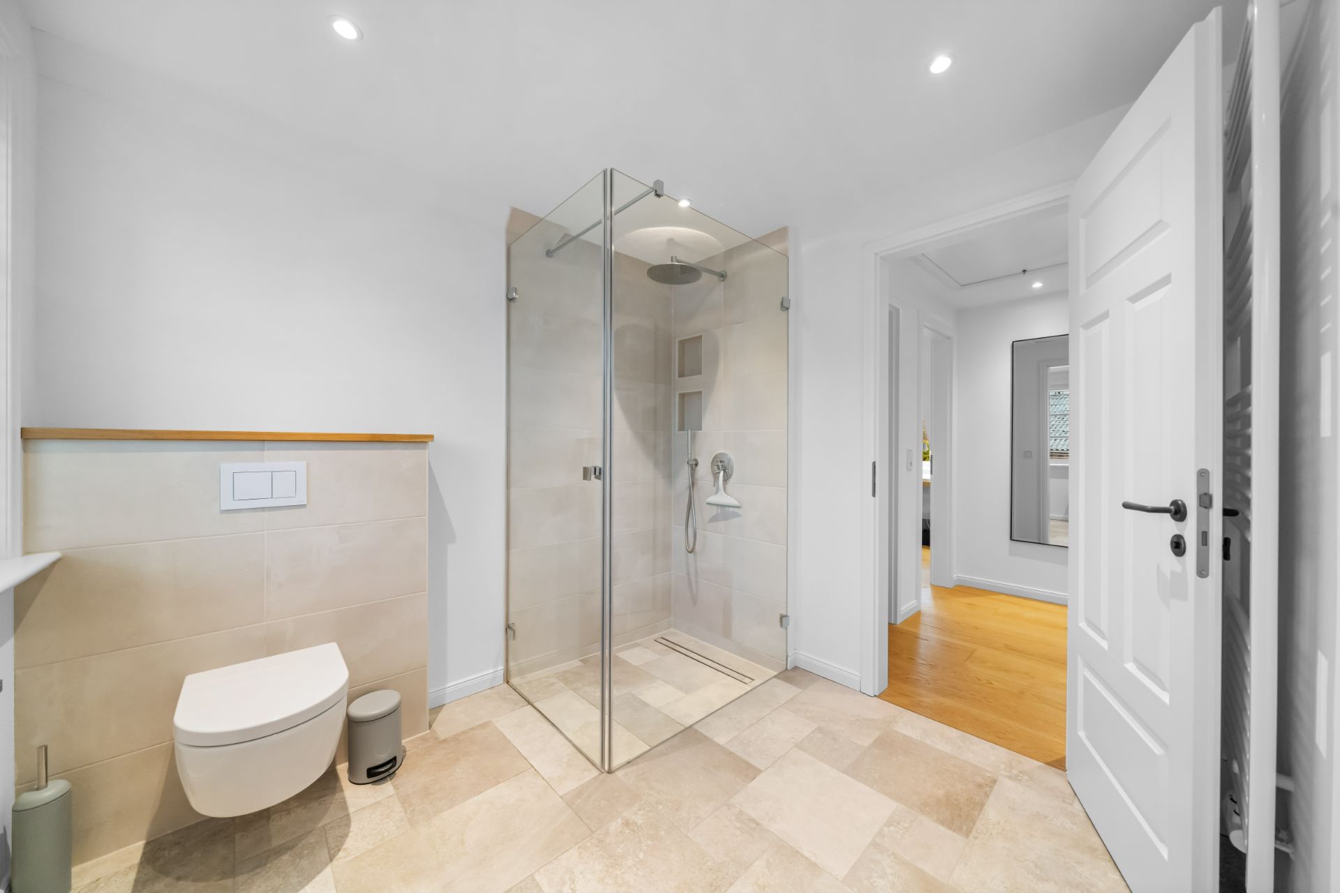 Modernes Bad mit großer Dusche aus Glas, Wandtoilette und Fliesenboden.
