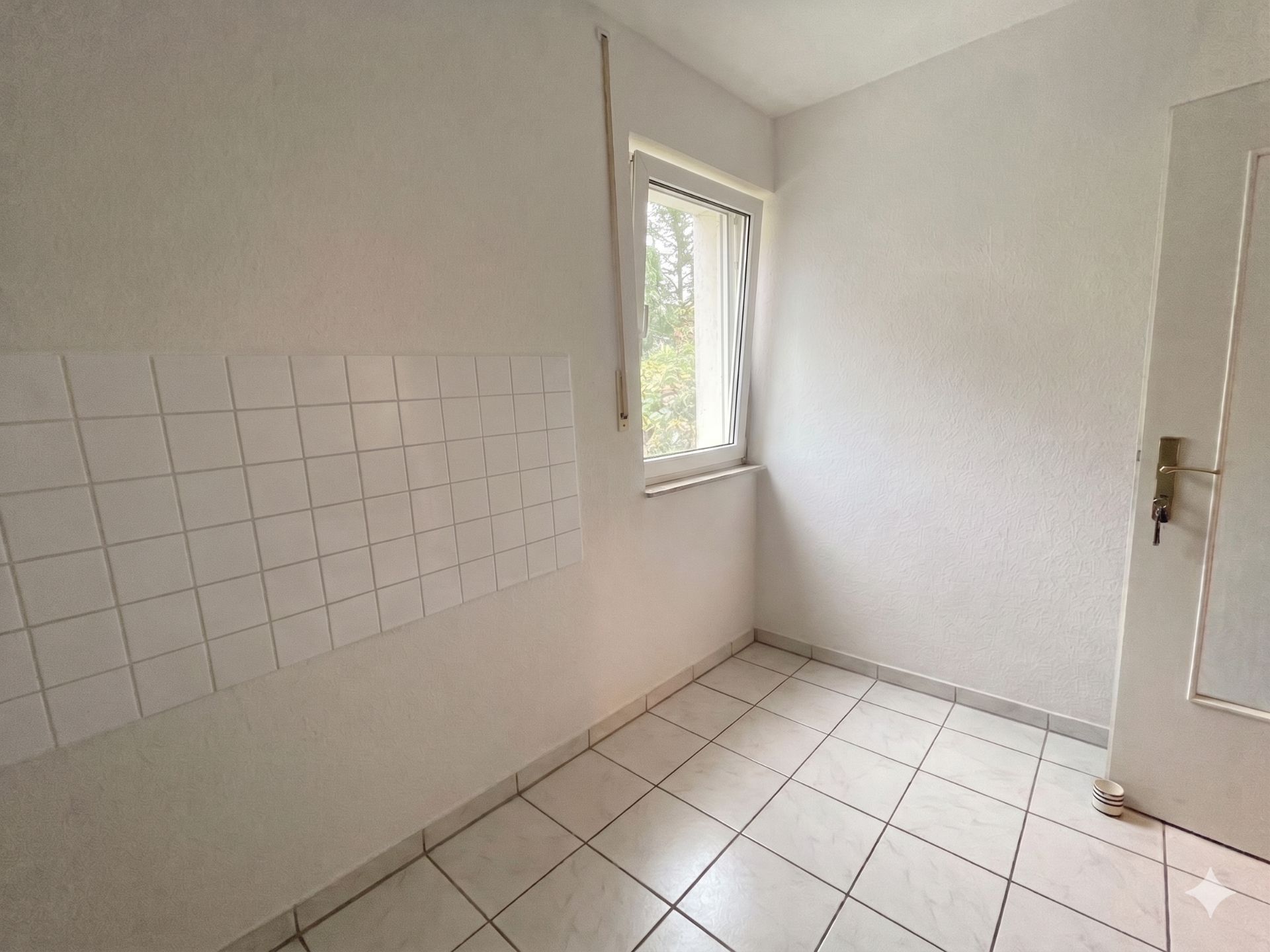Heller, leerer Raum mit weißen Fliesen, Fensternische und Tür.