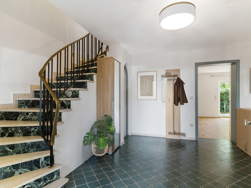Eingangsbereich mit grüner Marmortreppe, Fliesenboden, Garderobe und Pflanze in einem Haus.