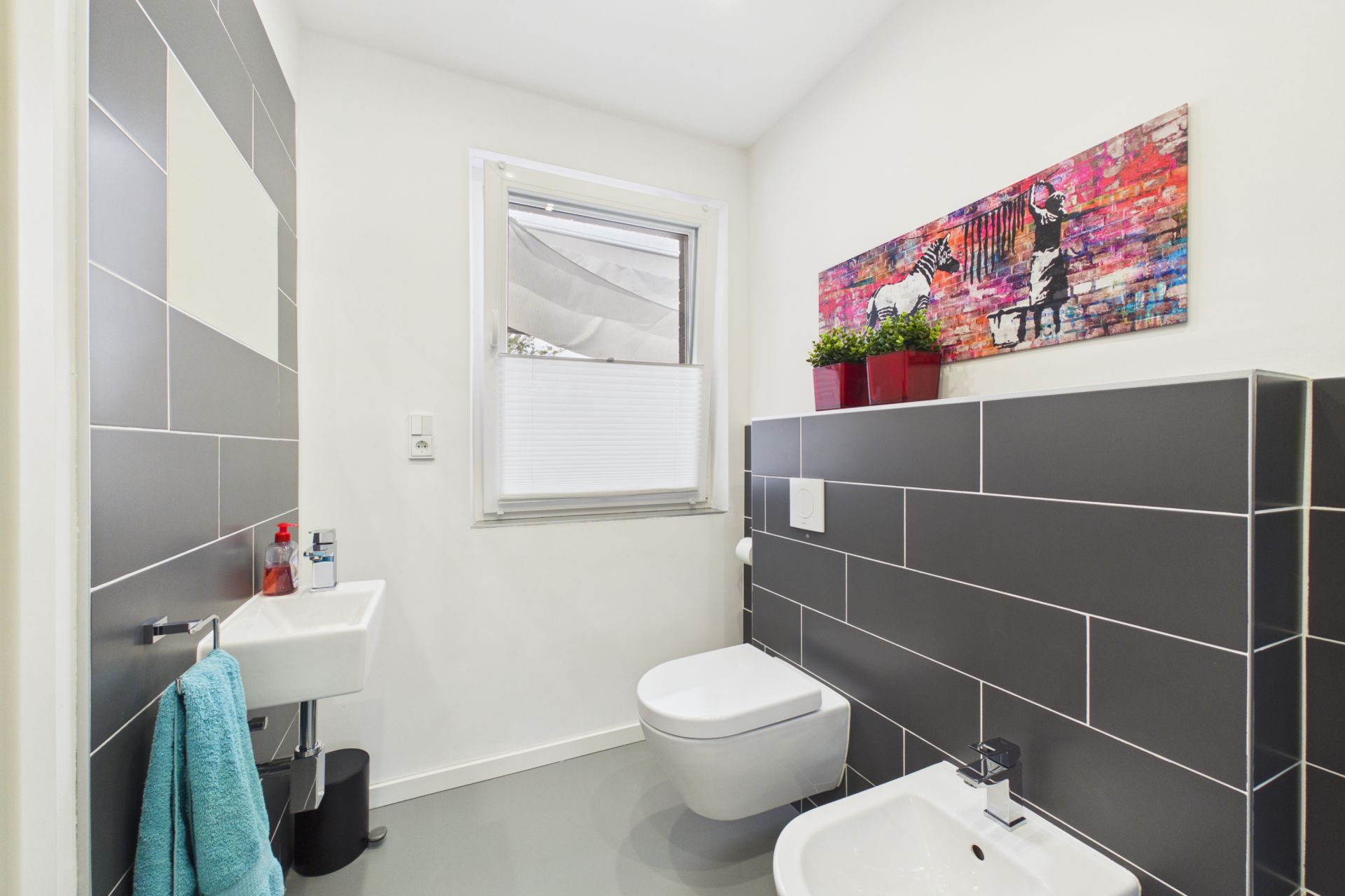 Modernes Badezimmer mit Wandtoilette, Bidet, kleinem Waschbecken und farbigem Wandbild.