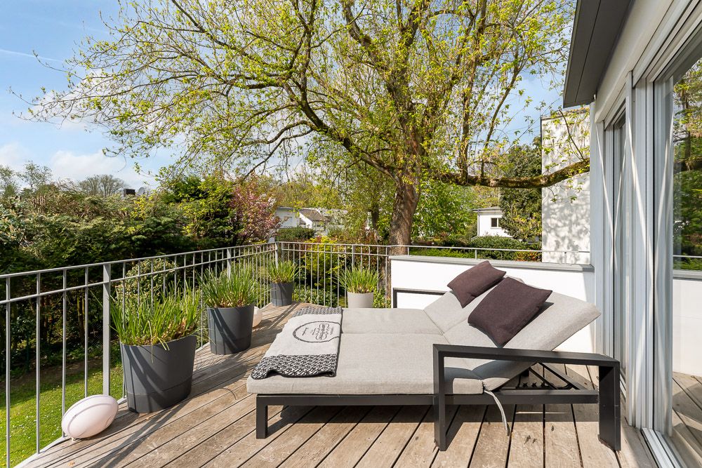 Große Terrasse mit Liege, Pflanzen in Töpfen und Blick auf Bäume und Garten.