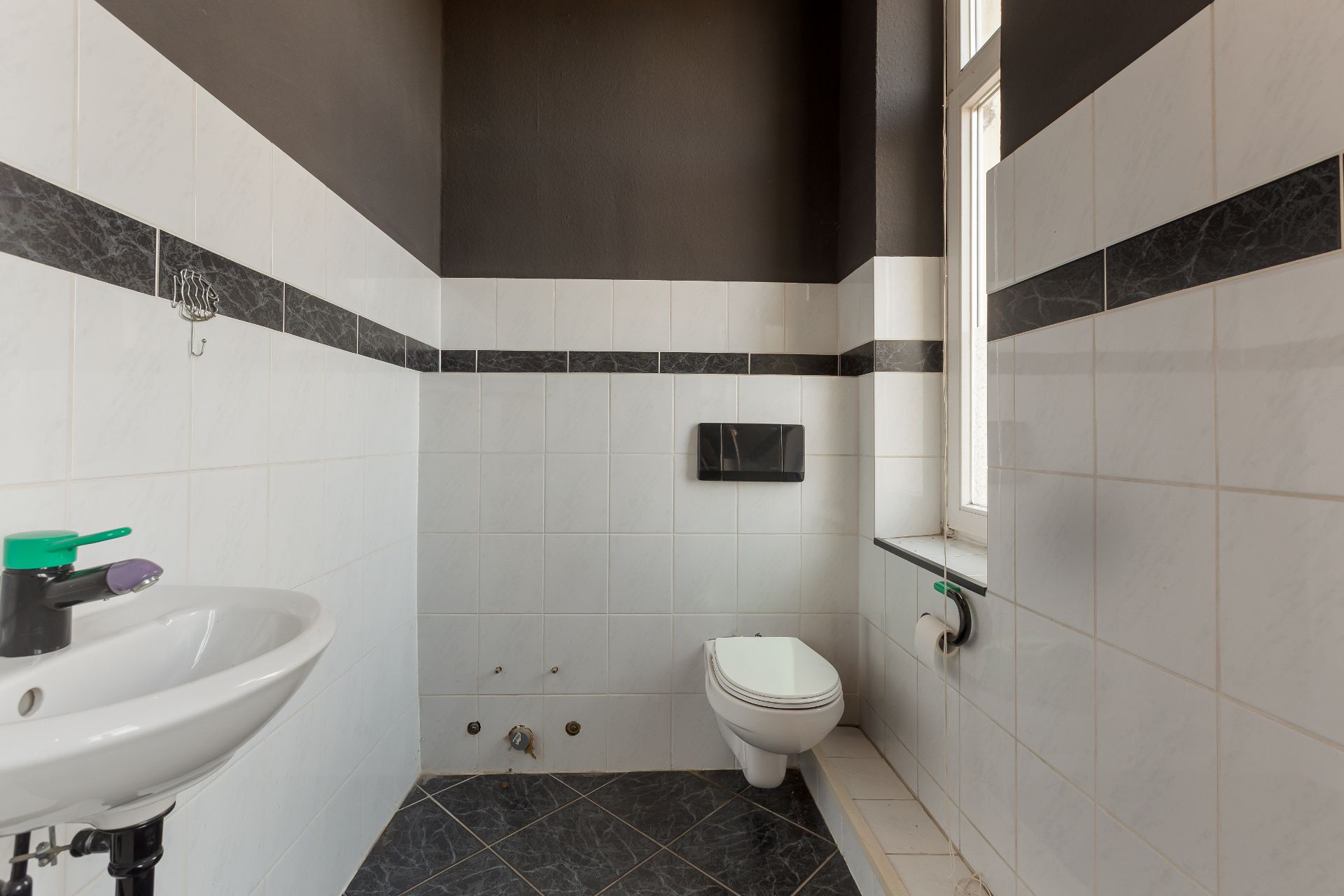 Modernes Badezimmer mit Wandtoilette, Waschbecken und Fenster, weiß-schwarz gefliest.