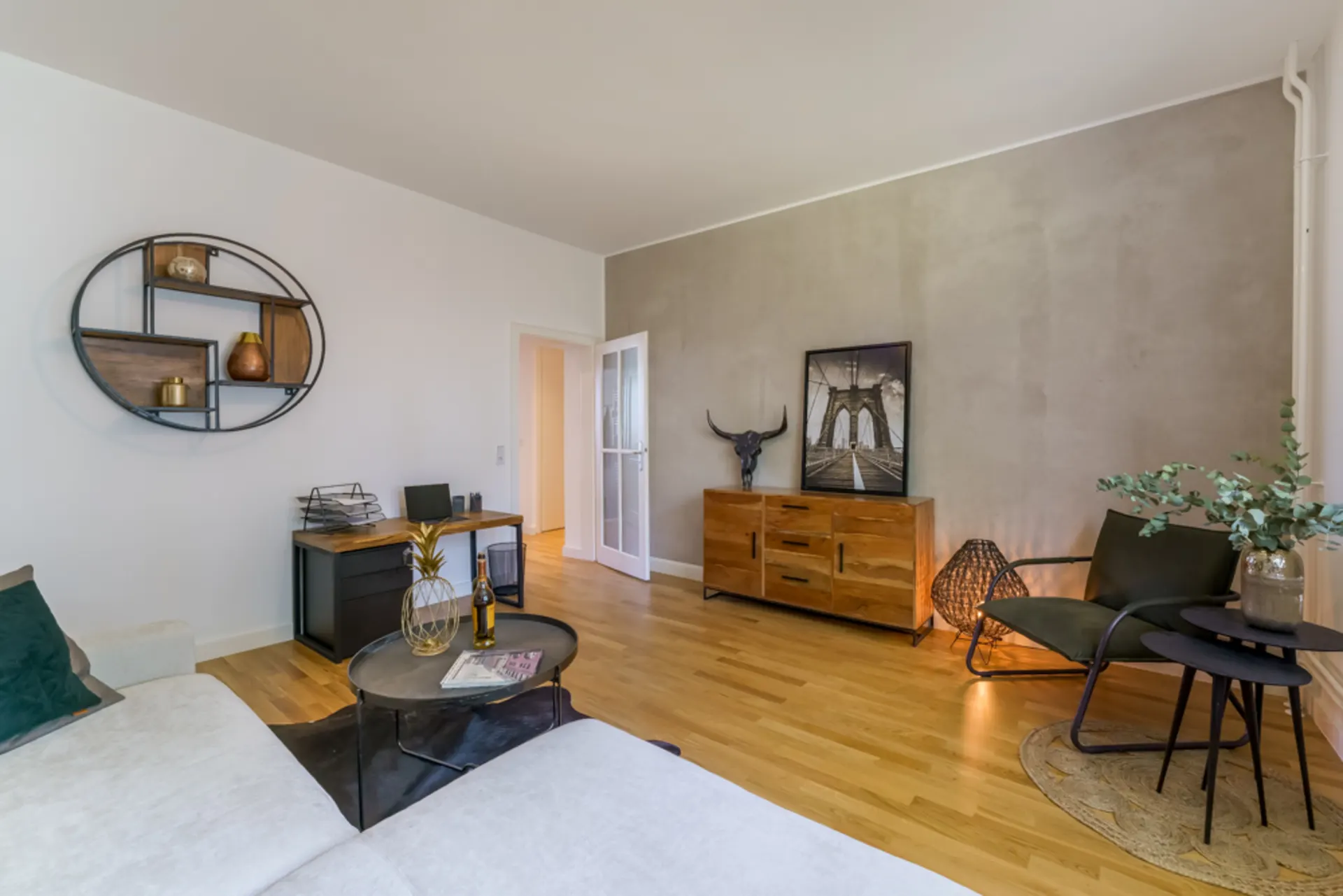 Modernes Wohnzimmer mit Holzfußboden, Sofa, Schreibtisch, Kommode und dekorativer Wandkunst.