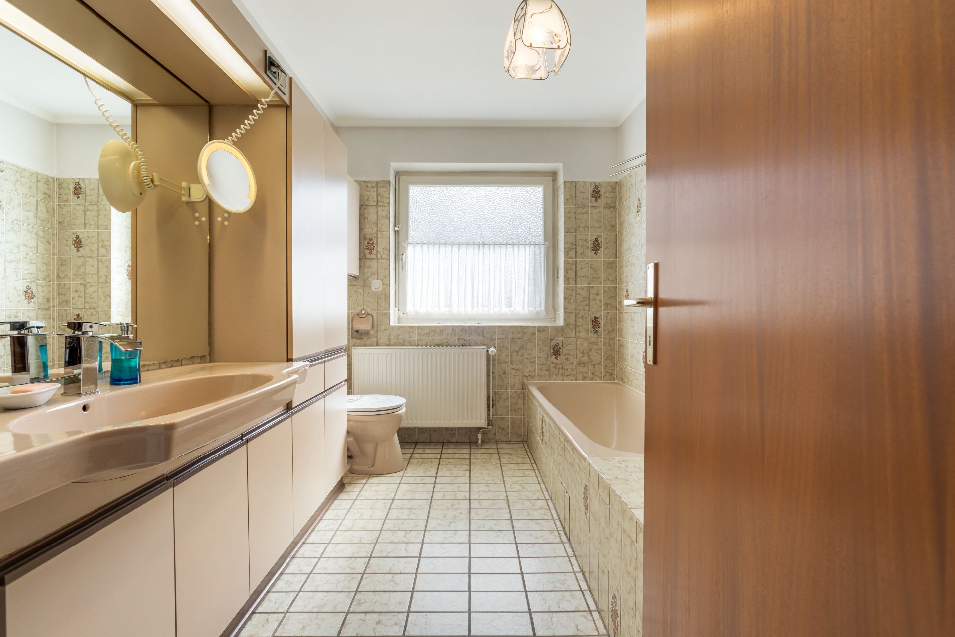 Badezimmer mit Waschbecken, Spiegel, Toilette, Badewanne und Fenster mit Vorhang.