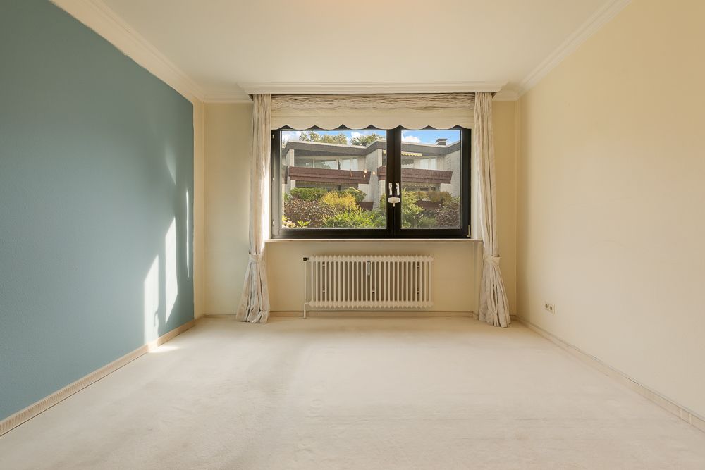 Leerer Raum mit hellen Wänden, einem Fenster mit Vorhängen und blau gestrichener Wand links.