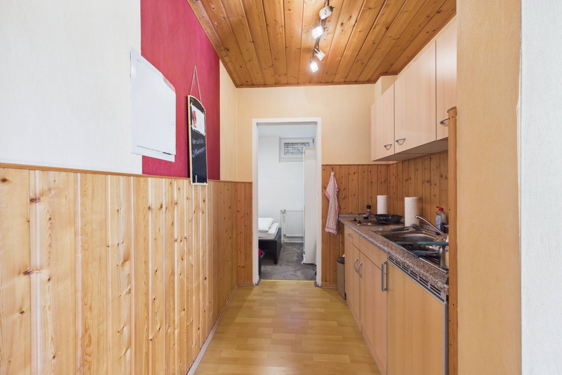 Schmale Küche mit Holzverkleidung, Holzdecke und Küchenzeile rechts, Tür zu anderem Raum am Ende.