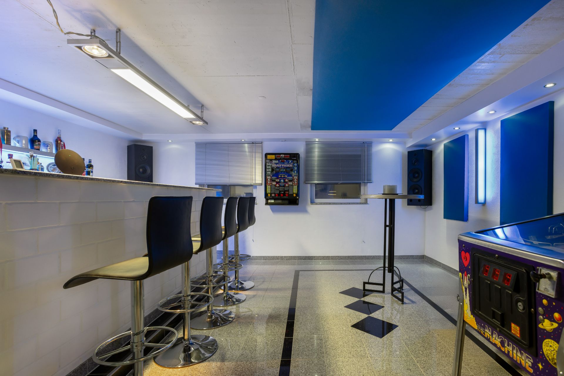 Wohnraum mit Bartresen, Barhockern, Flipperautomat und Wanddekoration.